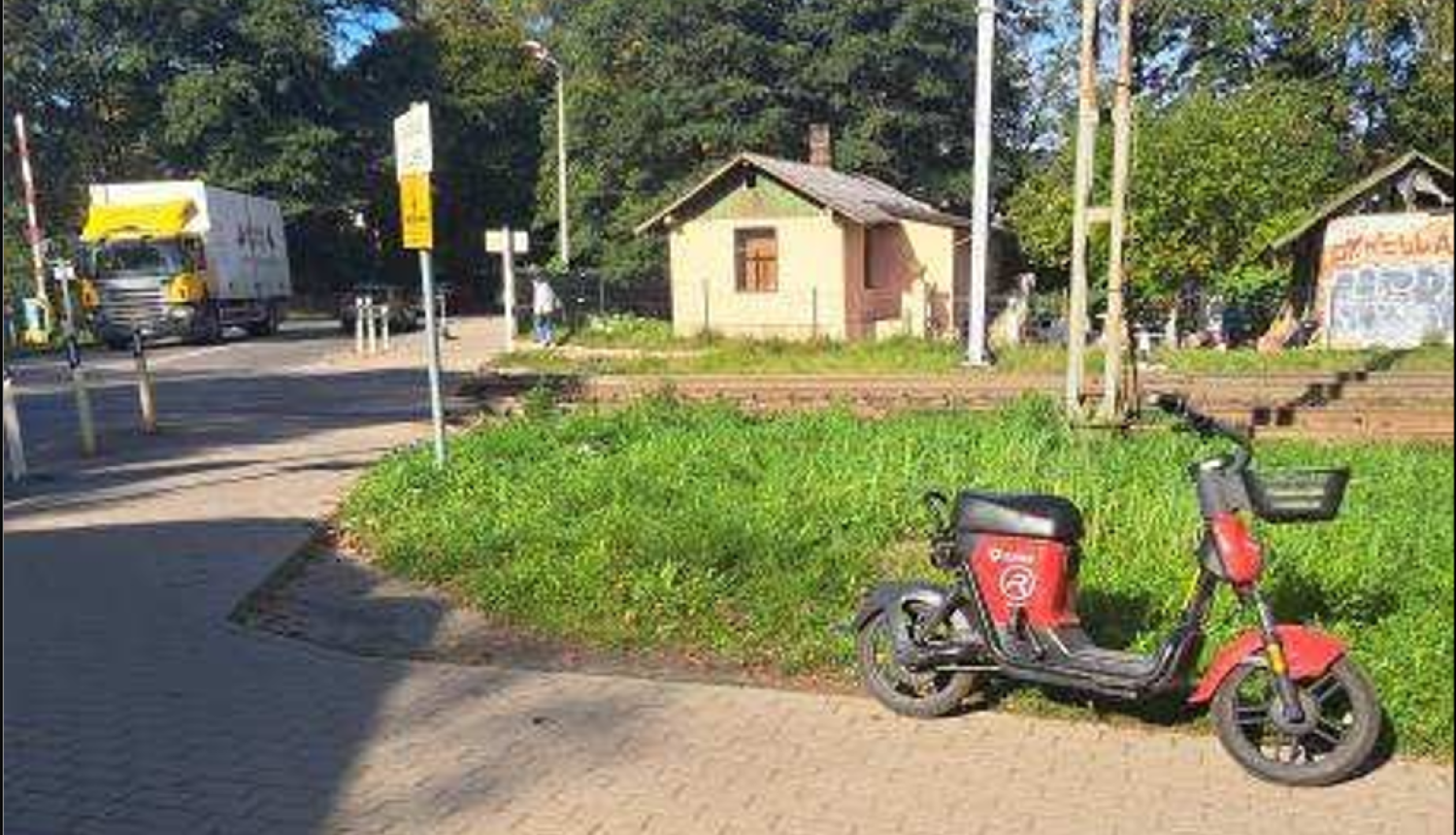Dzelzceļa pārbrauktuve pie kuras novietots elektriskais braucamrīks sarkanā krāsā