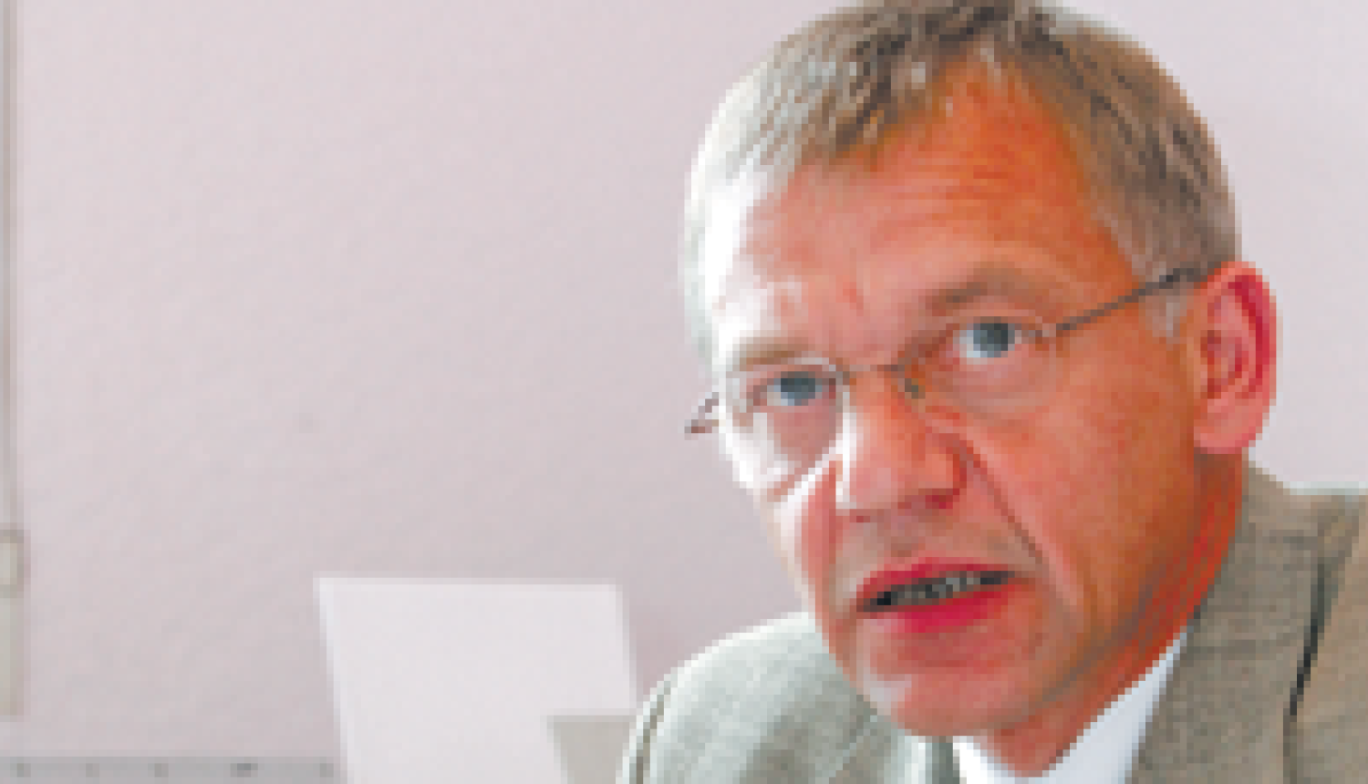 Vīrietis gaišā uzvalkā sēz pie rakstāmgalda